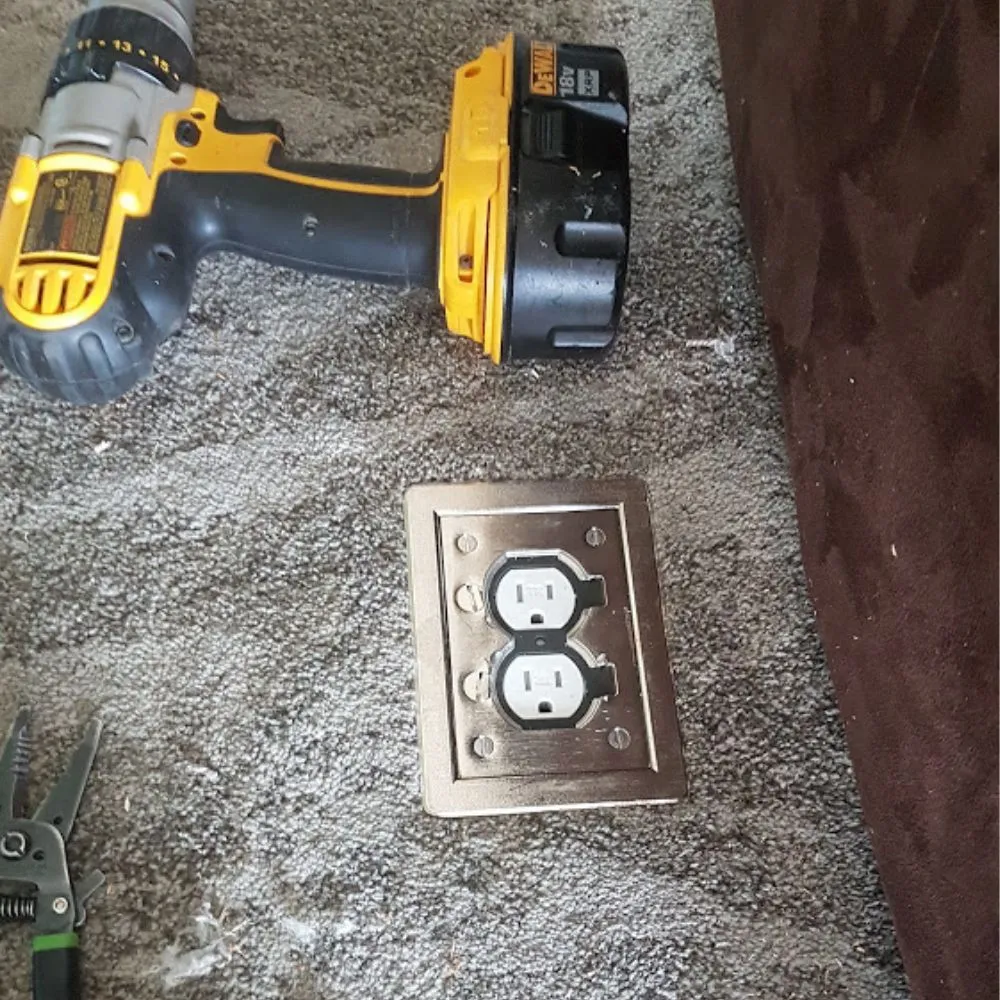 An electrical outlet installed in the floor with a yellow drill.